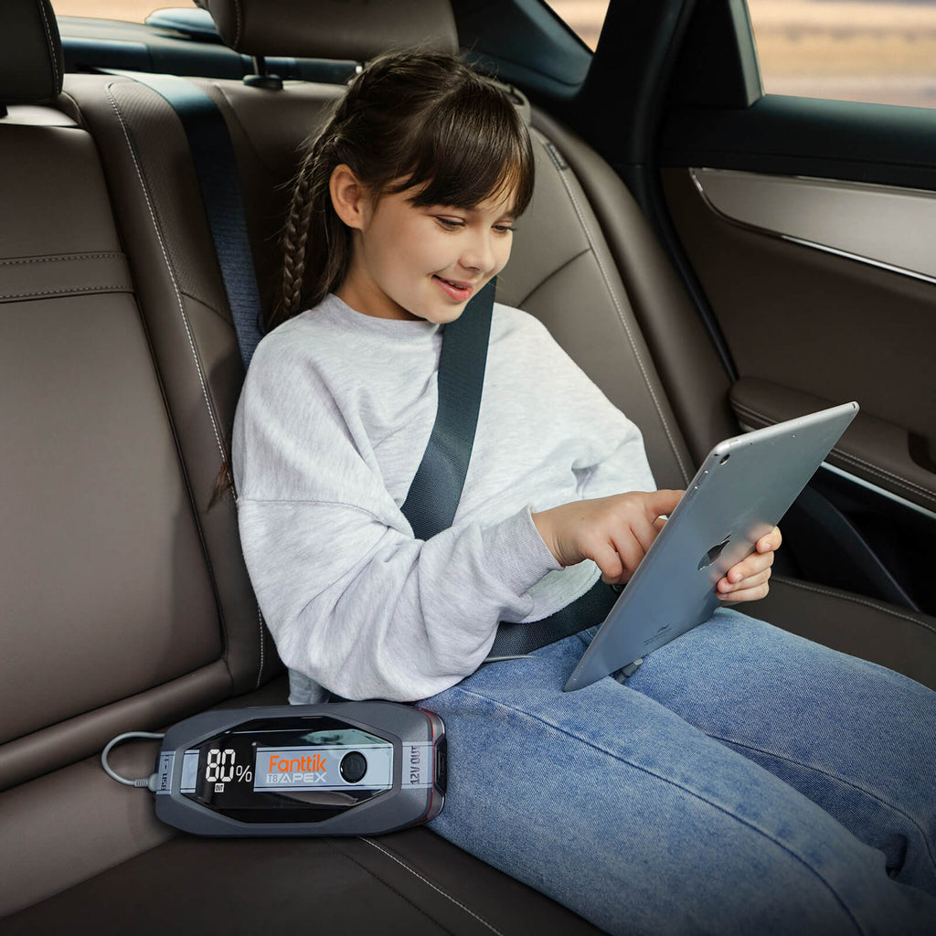 Young girl in the back seat of a car uses a tablet while a Fanttik T8 APEX jump starter with 80% charge is beside her.