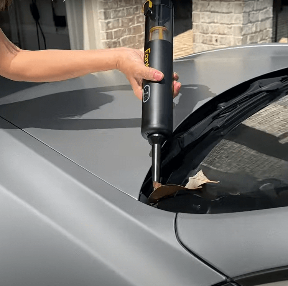 Fanttik Slim V8 Apex car vacuum cleaning leaves from car windshield crevice.