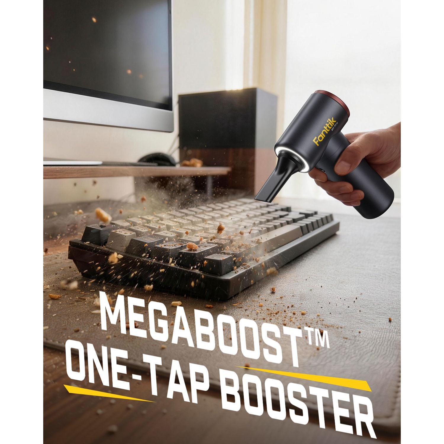 A hand holding a black Fomix Megaboost One-Tap Booster air duster, directing it toward a keyboard on a desk. Dust and debris are being blown up in the air.